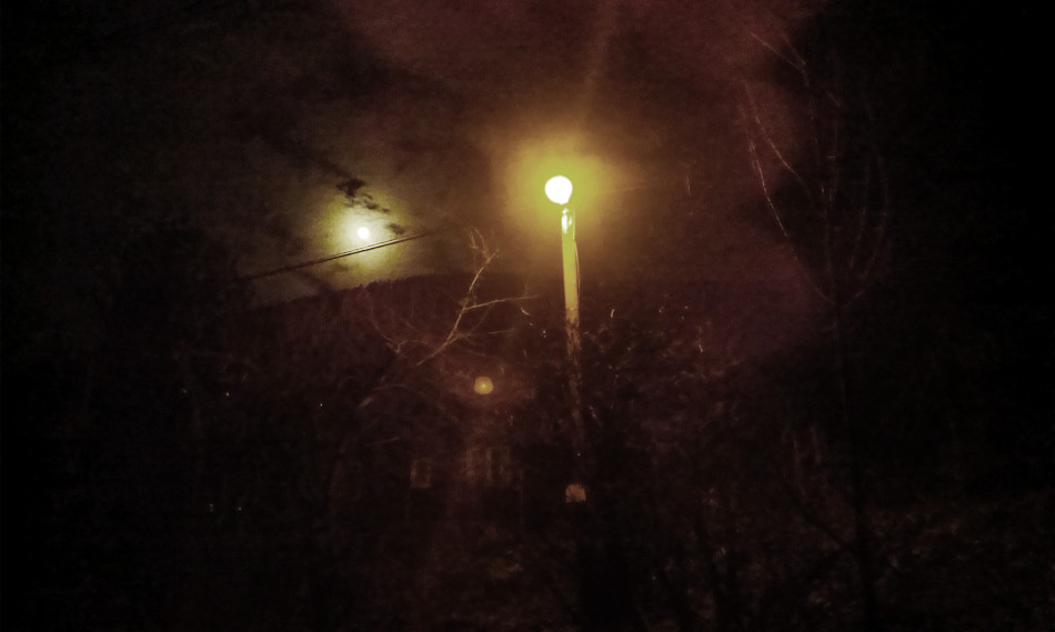 Měsíc, lampa a v dálce temný obrys hřebene.